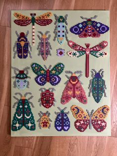 cross stitched bugs and dragonflies on a piece of white paper with wood flooring