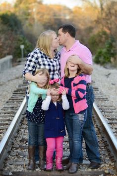 a man and two women kiss while standing on train tracks with their children in the foreground