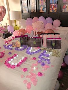 a bed topped with lots of pink and purple flowers next to balloons in the shape of letters