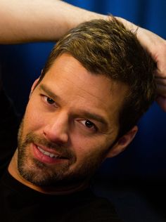 a close up of a person wearing a black shirt and holding his hand on his head