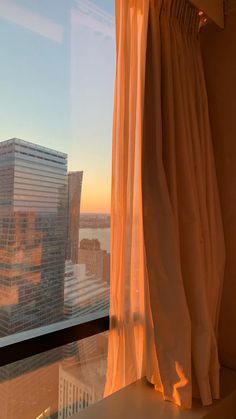 a window with curtains in front of a cityscape and skyscrapers at sunset