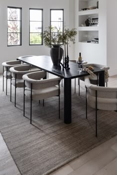 a dining room table with chairs and a vase on it in front of two windows