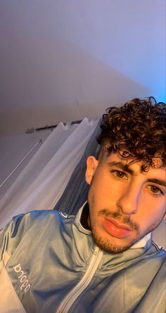 a man with curly hair wearing a blue jacket and looking at the camera while sitting down