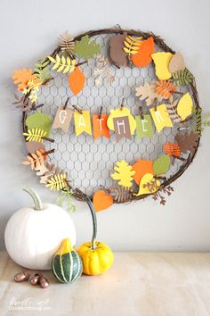 paper fall leaves wreath on a table with pumpkins and gourds next to it