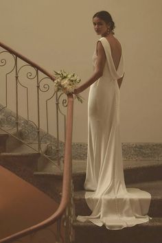 a woman in a white dress is standing on some stairs and holding a flower bouquet