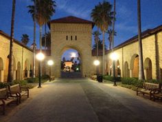 an archway between two buildings with benches and palm trees in the foreground at night