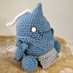 a crocheted blue stuffed animal sitting on top of a furry surface