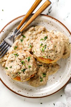 two biscuits covered in gravy on top of a plate next to a fork