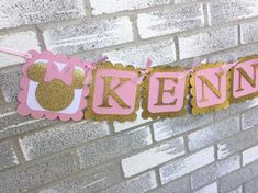 a pink and gold minnie mouse banner hanging on a brick wall next to a white brick wall