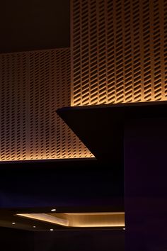 a clock is lit up in front of a wall with perfored panels on it