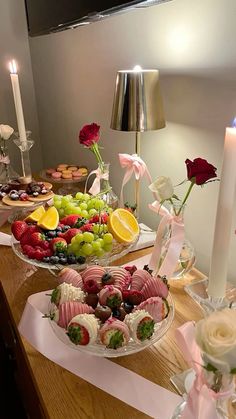 two trays filled with fruit and pastries on top of a wooden table next to candles