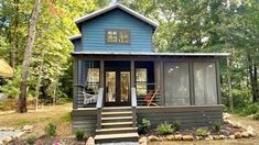 a small blue cabin in the woods with steps leading up to it's front door