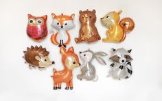 an assortment of foil balloons in the shape of animals on a white background with one balloon shaped like a fox, squirrel, raccoon, and other animal