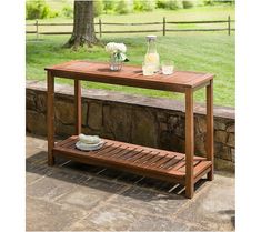 a wooden table sitting on top of a stone patio next to a tree and grass