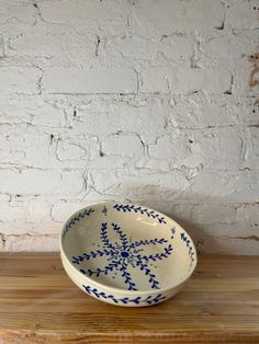 a blue and white bowl sitting on top of a wooden table next to a brick wall