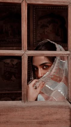 a woman is looking out the window with her veil over her head and wearing a wedding dress