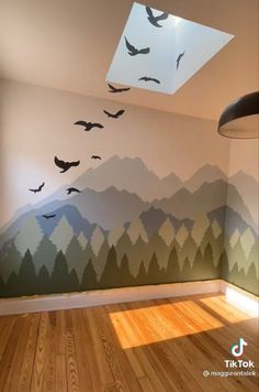 birds are flying in the sky above a mountain mural on a wall with wood floors