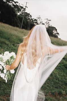 a woman in a white wedding dress holding a bouquet of flowers and wearing a veil