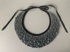 a black and silver beaded necklace on a white surface with a ribbon tied around it