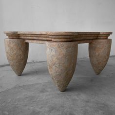 a large stone table with three legs on concrete floor next to white wall and cement flooring