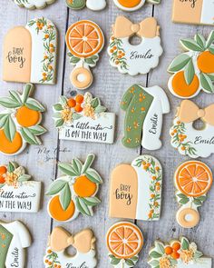 decorated cookies with oranges and greenery are arranged on a wooden surface, including one for the baby to be