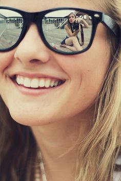 a woman wearing glasses with her reflection in the lens and smiling at the camera,