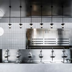 an industrial style kitchen with stainless steel fixtures and hanging lights above the counter area, along with wine glasses