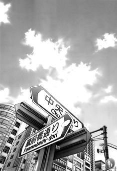 black and white photograph of street signs in front of buildings with cloudy sky behind them