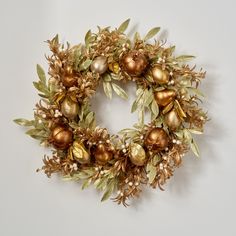 a wreath with gold and green ornaments hanging from it's sides on a white wall