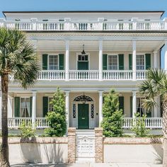 a large white house with green shutters and palm trees in front of the building