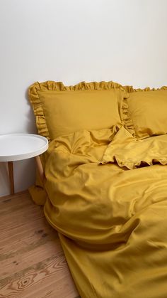 a bed with yellow sheets and pillows in a white room next to a wooden floor