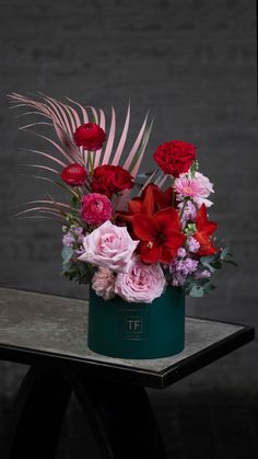 a green vase with red and pink flowers on a table in front of a brick wall