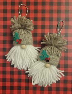 two knitted christmas ornaments hanging from hooks on a red and black checkered table cloth