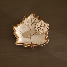 a white and gold leaf shaped dish sitting on top of a wooden table next to a brown wall