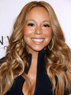 a woman with long blonde hair and big hoop earrings smiles at the camera while standing in front of a white wall