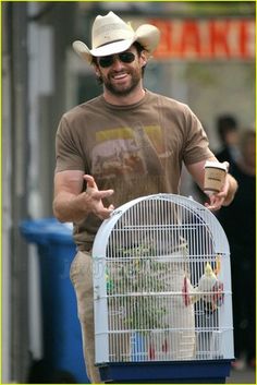 a man in a cowboy hat is holding a bird cage and pointing to the side