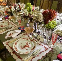 the table is set with red and white dishes, silverware, and wine glasses