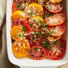 a white casserole dish filled with sliced tomatoes and parmesan cheese on top