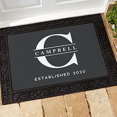 a black door mat with the words campbell established in white on it and a plant next to it