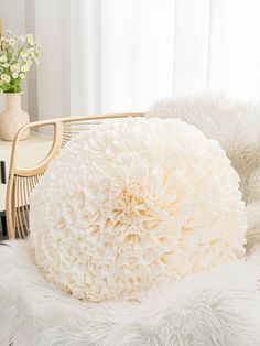 a white fluffy pillow sitting on top of a chair next to a vase filled with flowers