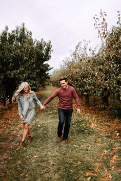 a man and woman holding hands walking through an apple orchard