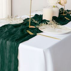 the table is set with white flowers and green cloths, gold candlesticks and greenery