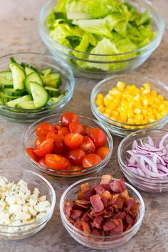 several bowls filled with different types of salads on a counter top next to cucumbers, tomatoes, corn and lettuce