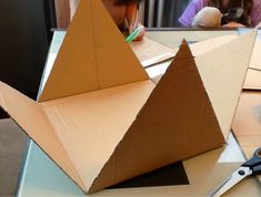 a cardboard pyramid sitting on top of a table next to scissors and a pencil in it