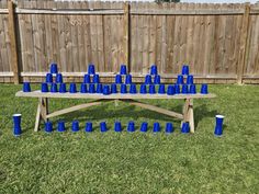 a wooden table with blue cups on it in the grass next to a wood fence