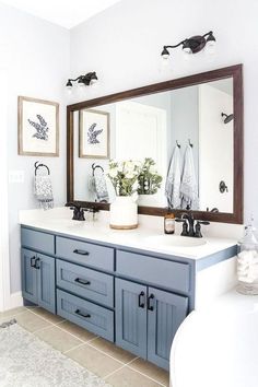 a bathroom with blue cabinets and white counter tops, two mirrors on the wall above it