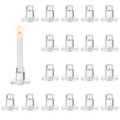 a lit candle surrounded by many small glass cups and saucers on a white background