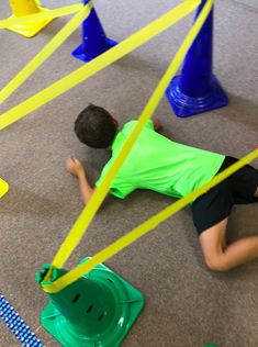 a young boy laying on the ground surrounded by plastic cones and caution tape as he plays with his toys