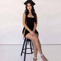 a woman sitting on top of a stool wearing a graduation cap