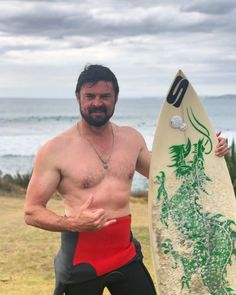 a shirtless man holding a surfboard in front of the ocean